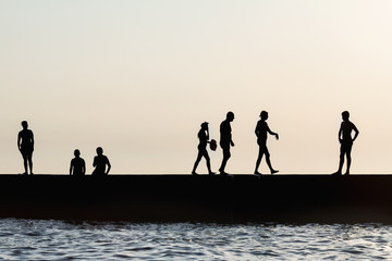 Silhouettes of people having a rest on a pier on the seashore. Rest on the sea beach.
