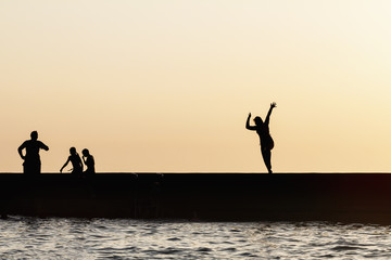 Silhouettes of people jumping from the sea pier. Rest on the sea beach