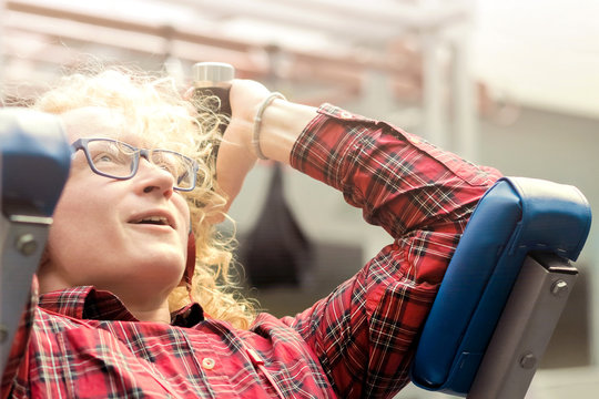 Gym. A skinny guy with glasses and headphones with curly blond hair. Close-up.