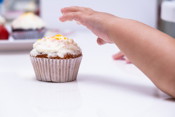 Childrens hand reaches for the cake. Cake. Cup cake on white table, on white background