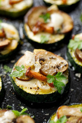 Zucchini pizza bites  from zucchini slices with the addition of brown mushrooms,  chanterelles, mozzarella cheese and herbs on a black background, top view, close-up. Vegetarian food