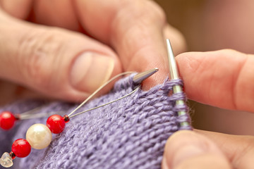 Woman is knitting a blue warm sweater. A hobby of elderly woman is knitting. Closeup view of knitting loop. Selective focus