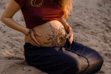 Pregnant woman with mehendi henna tattoo on her belly and hands, cropped image, hands on pregnant...