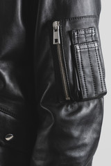 Leather black jacket with a pocket on zipper. Multifunctional pocket on an arm. Clothing background. Vertical photo.