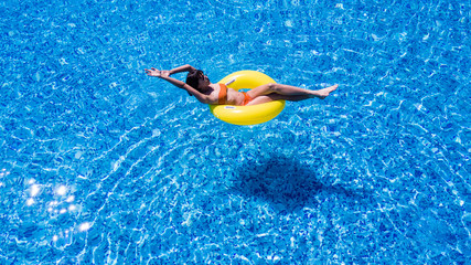 Beautiful young woman in hat in swimming pool aerial top view from above, girl in bikini relaxes and swims on inflatable ring has fun in water on family vacation