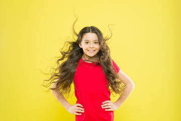 Teaching your child healthy hair care habits. Happy little girl child smiling with flowing long brunette hair on yellow background. Free child care. Pediatric health care