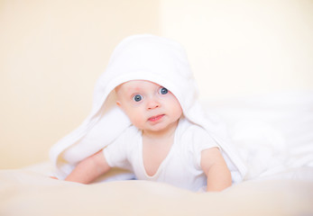 Cute little baby in white towel after bath on bed at home