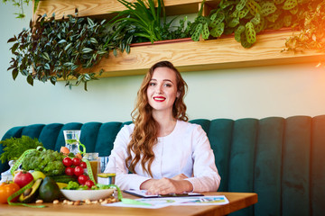 Portrait of a young woman nutritionist in medical gown sitting in the office with healthy food on...