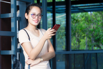 Copy space. Asian girl smiling wearing glasses standing using smartphone in the building shade. And the sunlight on.