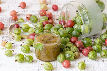 A small glass jar with homemade jam and the fresh gooseberry berries on an old table. Selective focus.