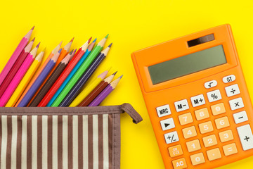 Color pencils in a school pencil case and a calculator on a bright paper yellow background. Office tools. education. top view.