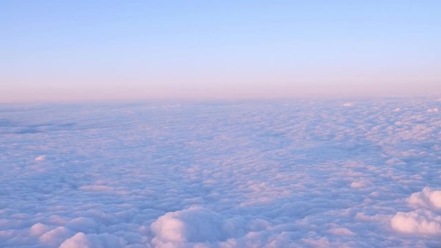 Beautiful clouds surface in sunset sky, view from plane during flight. Pink and blue cloudscape look like a snow.