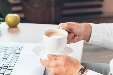 Young businessman working at laptop computer with hot coffee in hand.