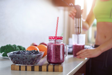 Sports healthy woman cooking fresh blueberry smoothie using hand blender at home. Healthy eating and berry drinks