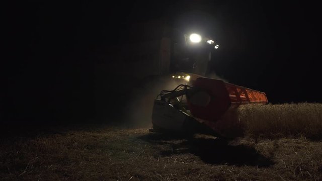 Harvesting works during the night, Full shot of the harvester with lights cutting the wheat