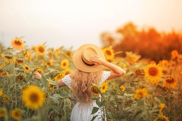 Beautiful curly young woman in a sunflower field holding a wicker hat. Portrait of a young woman in the sun. Summer.