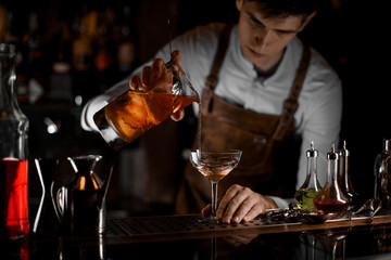 Bartender pouring alcohol cocktail from a strainer