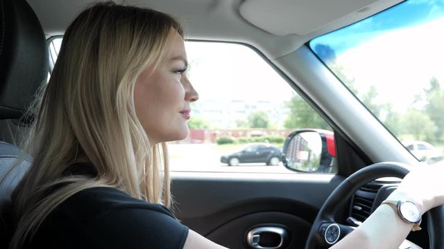 Portrait of female, side view. Woman driver on the road. Blonde young woman is driving a car in the city holding hands on steering wheel.