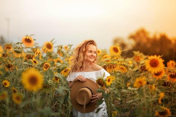 Beautiful curly young woman in a sunflower field holding a wicker hat. Portrait of a young woman in the sun. Summer.