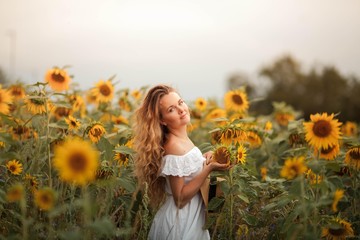 Fototapeta na wymiar Beautiful curly young woman in a sunflower field holding a wicker hat. Portrait of a young woman in the sun. Summer.