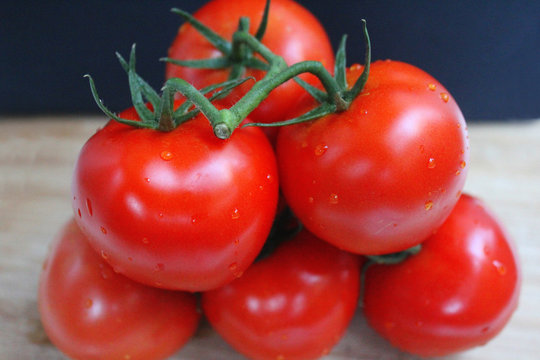 Ripe red cherry tomatoes on a twig on a wooden boadr in front of blue backdrop
