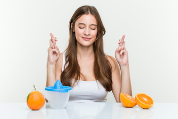 Young caucasian woman with an orange juicer crossing fingers for having luck