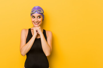 Young swimmer caucasian woman keeps hands under chin, is looking happily aside.