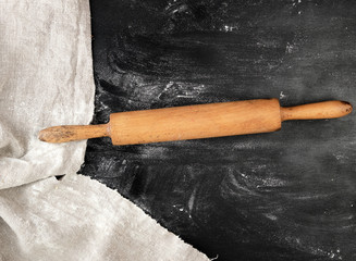 wooden rolling pin on a black background, white wheat flour