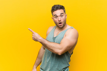 Young fitness man against a yellow background pointing to the side