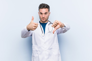 Young handsome doctor man showing thumbs up and thumbs down, difficult choose concept
