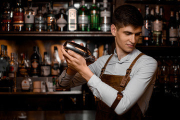 Portrait of young bartender in apron pouring cocktail
