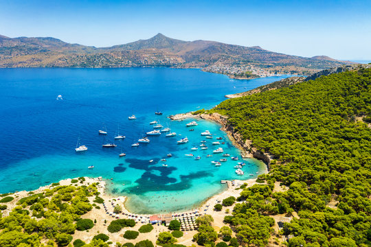 Der beliebte Strand auf der kleinen Insel Moni gegen&uuml;ber von Perdika bei &Auml;gina mit t&uuml;rkisem Meer und zahlreichen Segelbooten, Griechenland