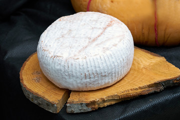 Fototapeta na wymiar Big head of cheese in a white mold lying on a wooden board, black backgraund