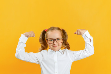 Little girl in a white shirt and glasses. The child shows strong hands. The concept of education, school, success, girl power, feminism.