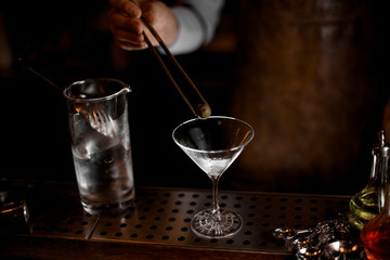 Bartender adds olive in martini with forceps