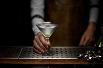 Bartender holds glass with martini on counter