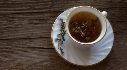a white Cup of herbal tea with a bunch of fresh wild thyme on an old wooden background