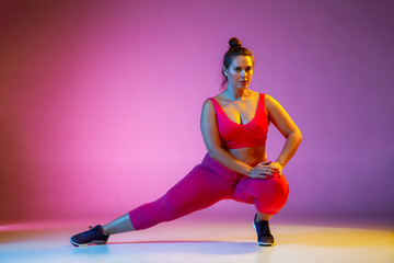 Young caucasian plus size female model's doing exercises on gradient purple background in neon...