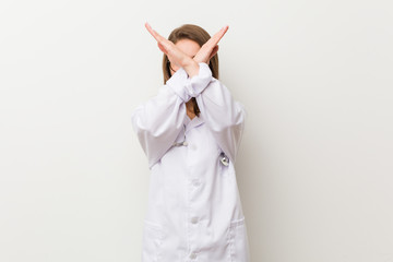 Young doctor woman against a white wall keeping two arms crossed, denial concept.