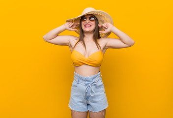 Young caucasian woman wearing a straw hat, summer look covering ears with hands.