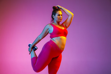 Young caucasian plus size female model's doing exercises on gradient purple background in neon light. Training in stretching. Concept of sport, healthy lifestyle, body positive, equality.