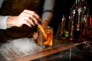 Bartender puts orange zest in whiskey glass