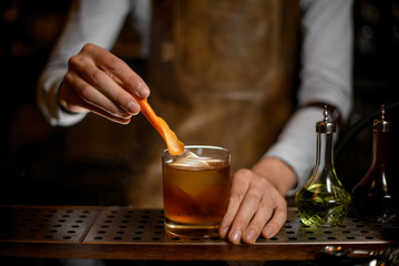 Bartender putting orange zest in whiskey glass