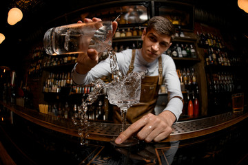 Young bartender pouring cocktail from the jar