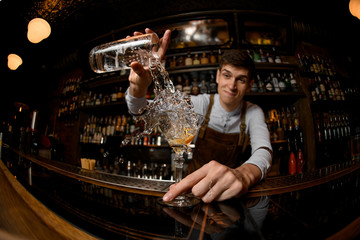 Young bartender pours alcohol from a jar