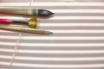 Watercolor brushes on a sheet of watercolor paper in the shadows of the blinds.
