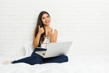 Young arab woman working with her laptop on the bed raising both thumbs up, smiling and confident.