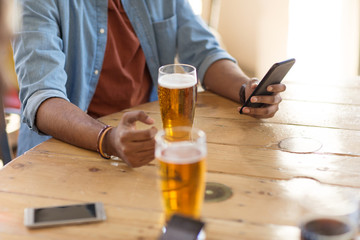 people and technology concept - man with smartphone drinking beer and reading message at bar or pub