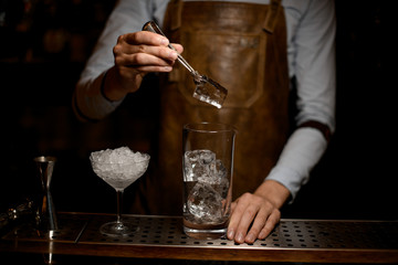 Bartender puts ice in cocktail glass with tongs