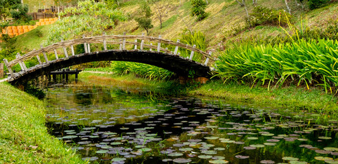 Arched wooden bridge over small lake.